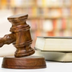 Martelo de juiz em madeira sobre base, com livros ao fundo, simbolizando justiça e lei.