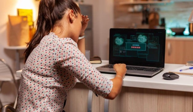 Mulher frustrada com acesso negado no laptop, tela exibe 'acesso negado'.