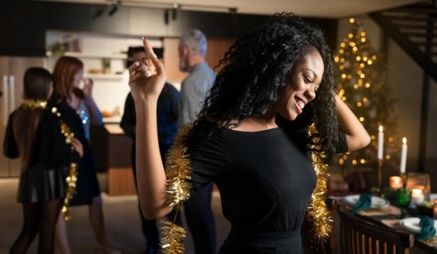 Mulher negra sorrindo dançando em uma festa com decoração festiva.