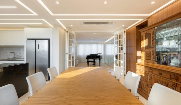 Sala de jantar elegante com mesa de madeira, cadeiras e piano ao fundo.