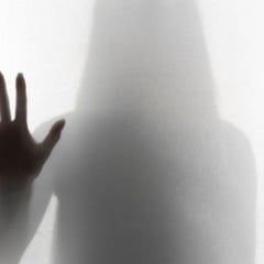 Sombra de pessoa atr&aacute;s de um tecido branco, m&atilde;o estendida em sinal de parada.