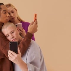 Tr&ecirc;s pessoas olhando para seus telefones, posando em um fundo bege.