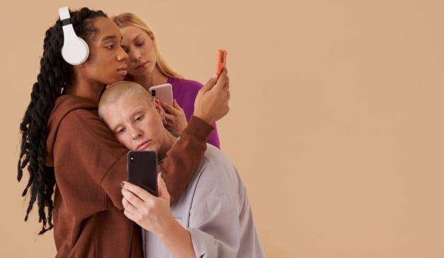 Três pessoas olhando para seus telefones, posando em um fundo bege.