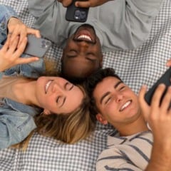 Grupo de amigos sorrindo e olhando para seus celulares em um piquenique.