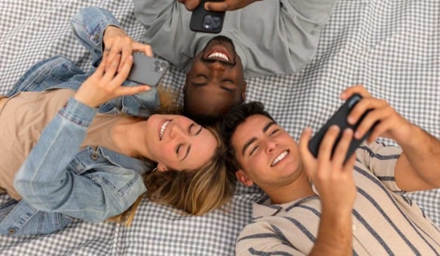 Grupo de amigos sorrindo e olhando para seus celulares em um piquenique.