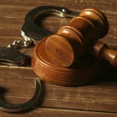 Imagem de um martelo de madeira e algemas sobre uma superf&iacute;cie de madeira.