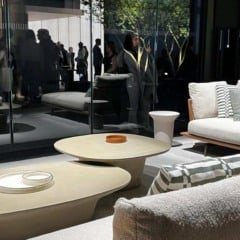 Interior de sala de estar moderna com m&oacute;veis elegantes, mesas de centro e pessoas ao fundo.