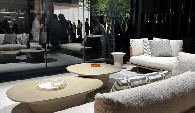 Interior de sala de estar moderna com móveis elegantes, mesas de centro e pessoas ao fundo.