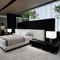 Quarto moderno com cama de design, cabeceira alta, e janela com vista para &aacute;rvores.