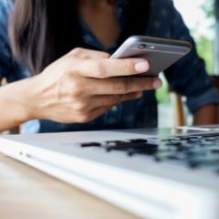 Uma pessoa usando um smartphone em cima de uma mesa com um laptop.