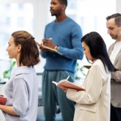 Grupo de pessoas em reuni&atilde;o de trabalho, com cadernos e roupas formais.