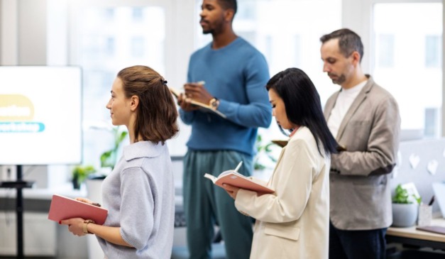 Grupo de pessoas em reunião de trabalho, com cadernos e roupas formais.