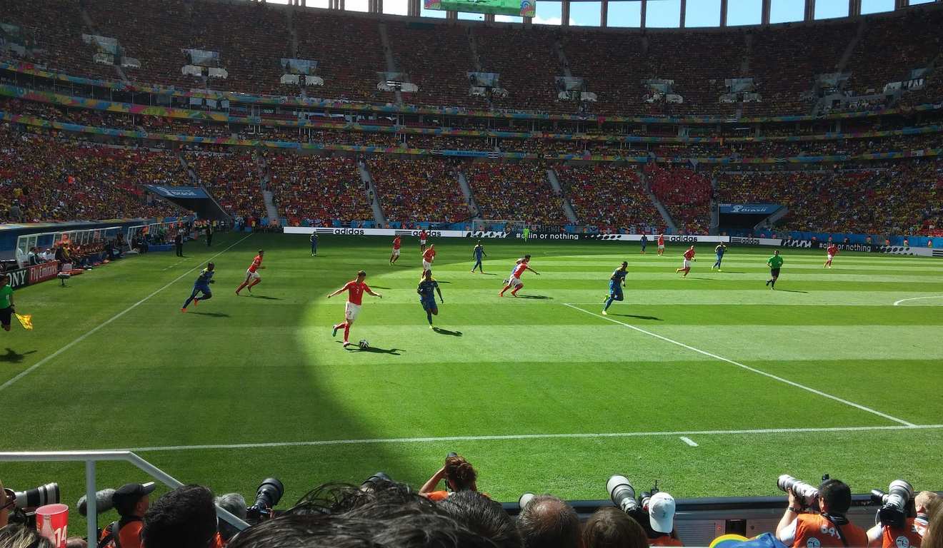 Jogo de futebol em estádio lotado. Jogadores correndo em campo verde. Jogo de futebol em estádio lotado. Jogadores correndo em campo verde.